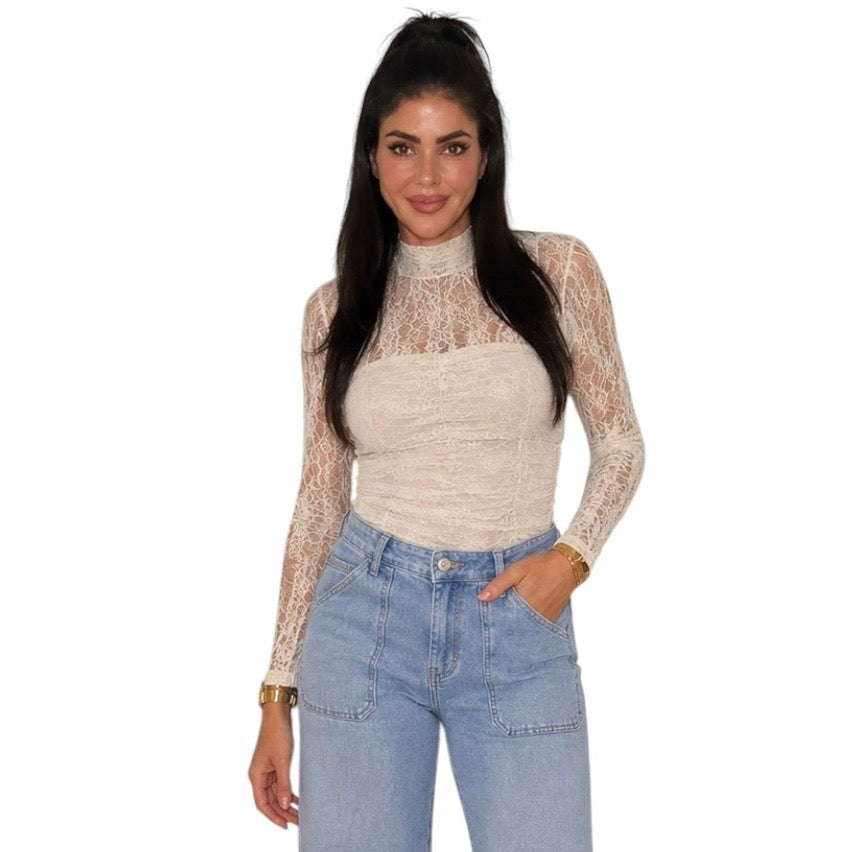 A woman modeling a beige lace long-sleeve mock neck top with a solid bandeau-style front panel, paired with light blue jeans, against a plain white background.