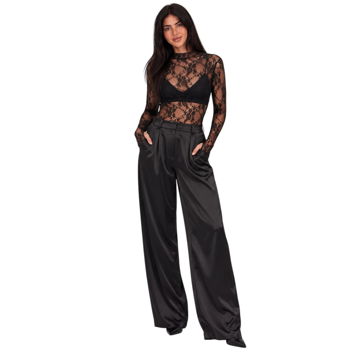 A woman modeling a black sheer lace long-sleeve crop top paired with high-waisted black satin wide-leg trousers, shown against a plain white background.