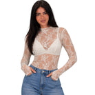 A woman modeling a sheer white floral lace long-sleeve top over a white bralette, paired with blue jeans, against a plain white background.