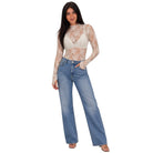 A woman modeling a sheer beige lace long-sleeve crop top paired with high-waisted, wide-leg blue jeans against a plain white background.