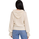A woman viewed from the back wearing a cream-colored knit hoodie with a lace-trimmed hood and lace-up cuffs, paired with blue jeans, against a plain white background.