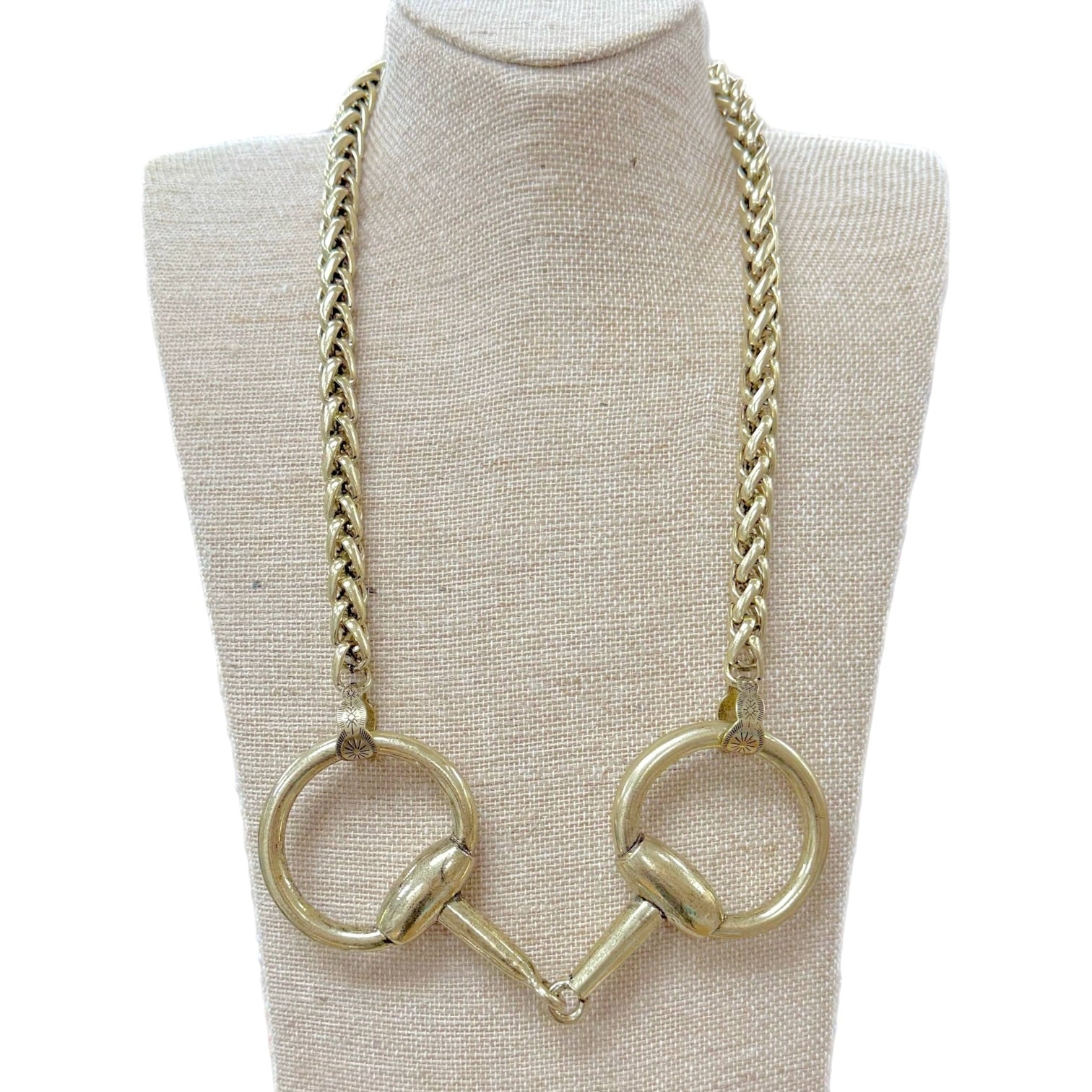 A gold-tone chain necklace with two large circular horse-bit style rings at the bottom, displayed on a beige fabric mannequin bust against a white background.