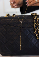 Black quilted handbag with a gold chain necklace draped over it.