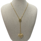 A gold lariat-style necklace displayed on a beige fabric-covered jewelry bust. The necklace features a delicate chain, a small oval medallion, and a long drop ending in a heart-shaped cluster of clear rhinestones.
