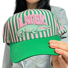 Green and pink striped cap with alligator logo held by a person