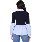 A woman shown from the back wearing a color-blocked long-sleeve blouse with a dark navy upper section, a light blue collar, and a light blue peplum hem, paired with blue jeans against a plain white background.