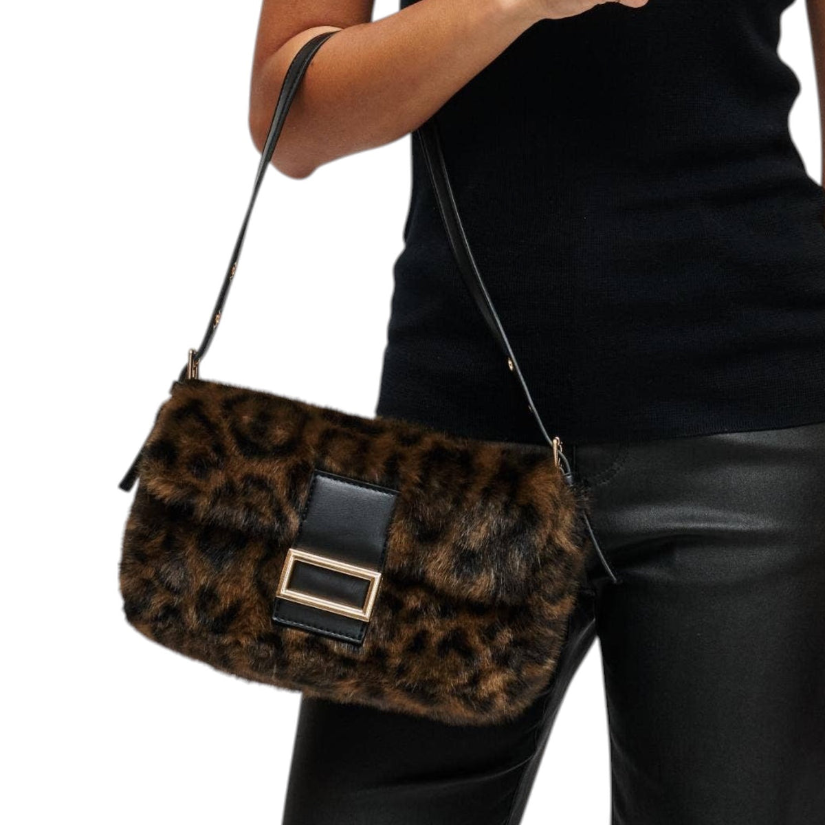 A leopard-print faux fur shoulder bag with black leather trim and a gold-tone buckle, shown being worn by a model in a black top and black pants against a white background.
