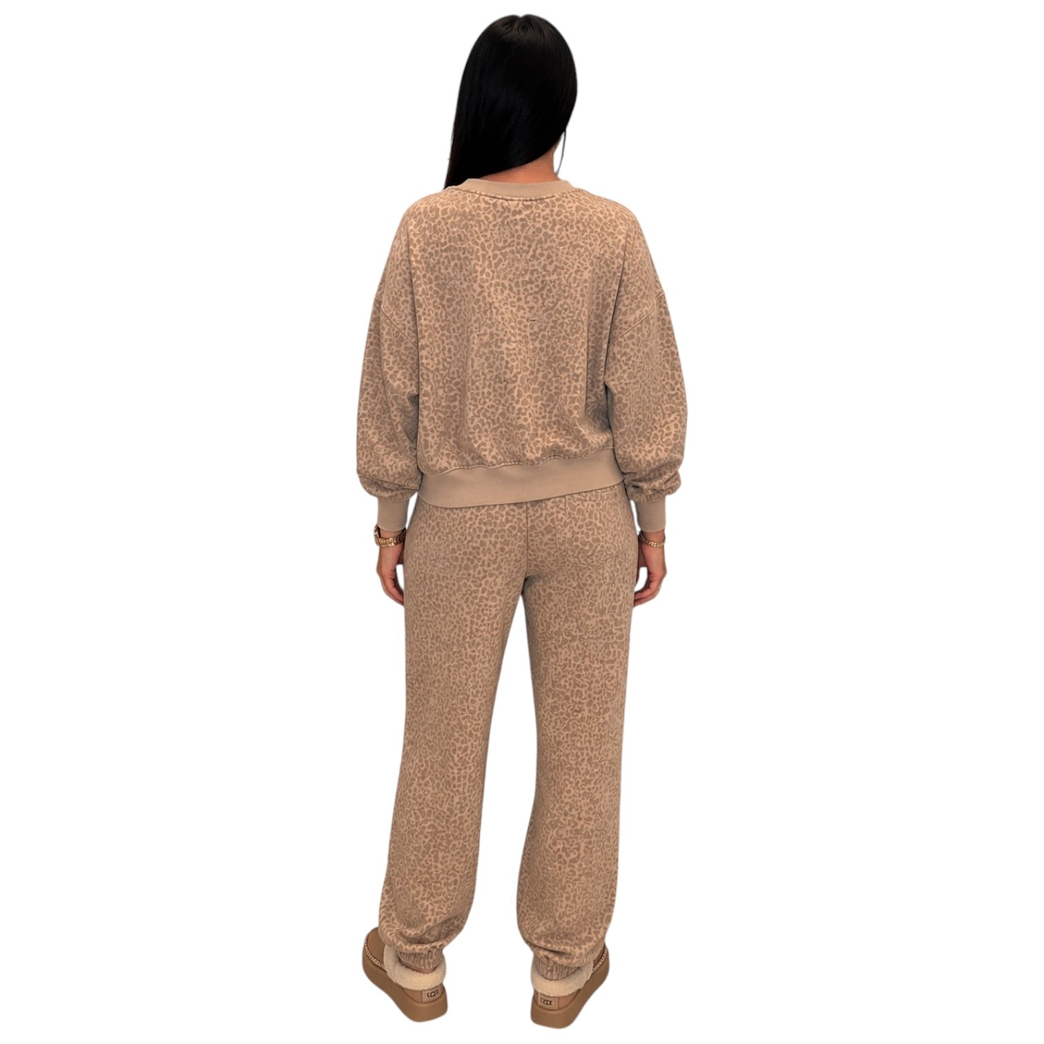 A woman shown from the back wearing a matching beige and brown leopard-print lounge set, consisting of a long-sleeve sweatshirt and jogger pants, on a solid white background.