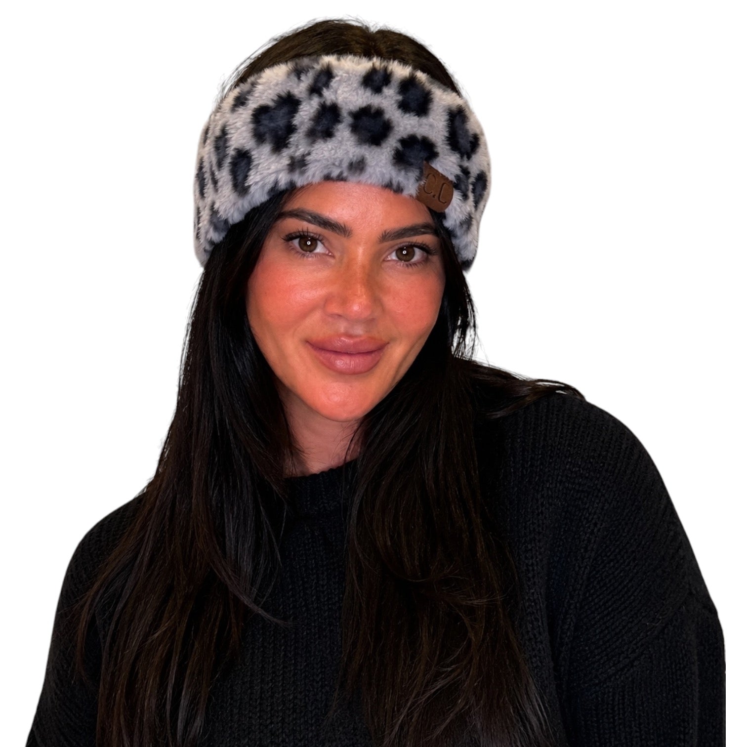 A woman wearing a gray faux-fur headband with a black leopard print pattern and a small brown leather logo tab, paired with a black knit sweater against a plain white background.