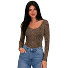 A woman modeling a long-sleeve scoop-neck top with a brown and black leopard print pattern, paired with blue jeans, against a plain white background.