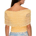 Woman wearing a yellow lace top with denim shorts on a white background