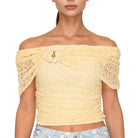 Woman wearing a yellow off-shoulder top with lace details on a white background