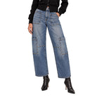 A model wearing a pair of wide-leg blue denim cargo pants with large patch pockets on the thighs and knees, styled with a black long-sleeve top and black pointed-toe heeled ankle boots against a plain white background.