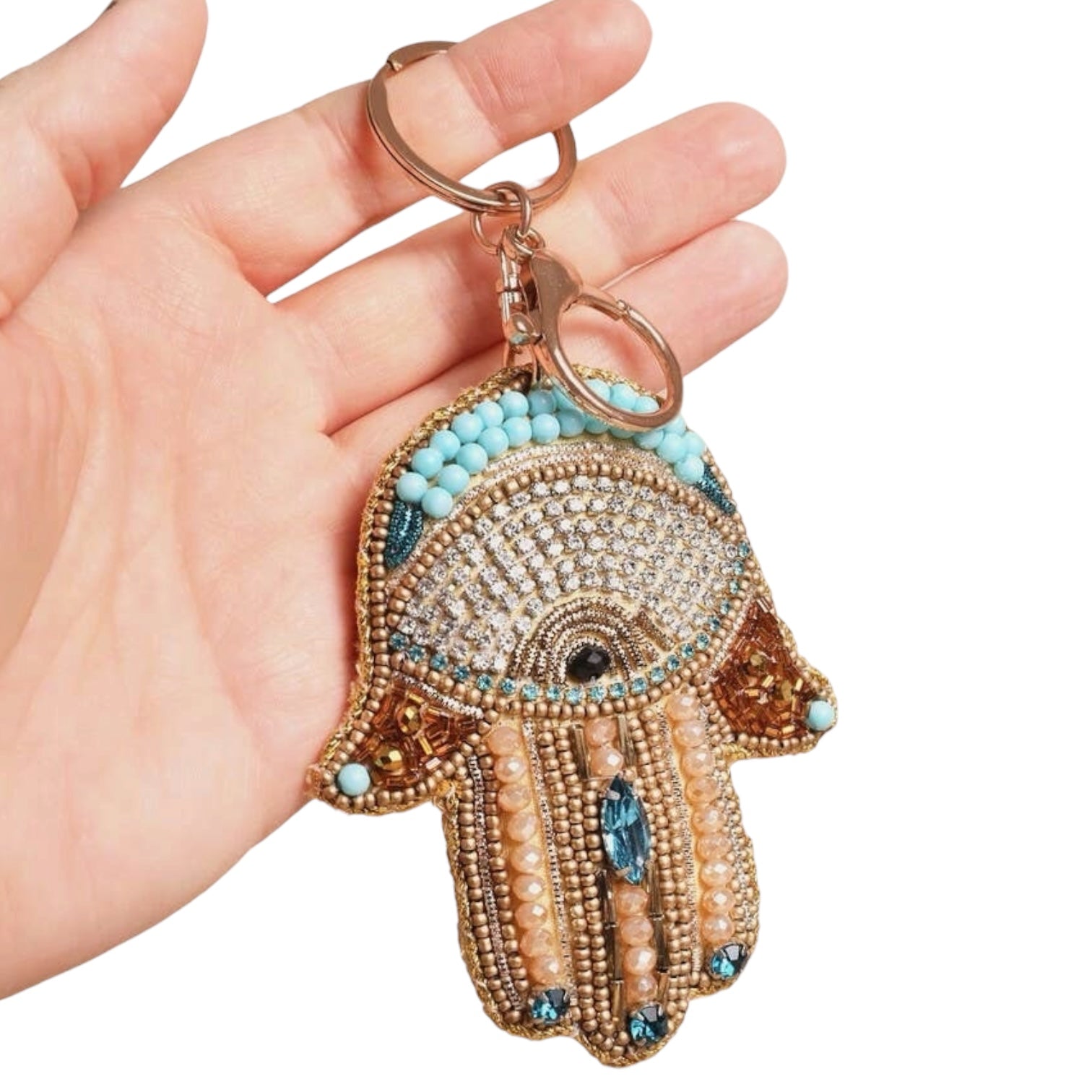 Hand holding a decorative Hamsa keychain with turquoise stones on a white background