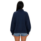A woman viewed from the back wearing an oversized navy blue sweatshirt and light blue denim shorts against a plain white background.
