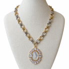 A two-tone gold and silver chain necklace with a circular pendant featuring a white religious image surrounded by clear rhinestones, displayed on a cream fabric mannequin bust.