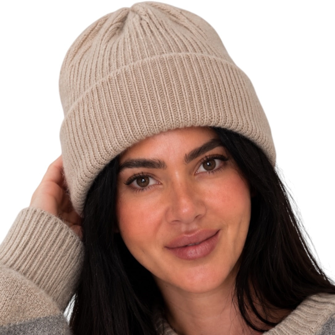 A woman wearing a beige ribbed knit beanie and a gray and beige argyle sweater, posing against a solid white background.