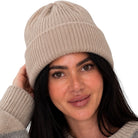 A woman wearing a beige ribbed knit beanie and a gray and beige argyle sweater, posing against a solid white background.