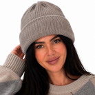 A woman wearing a light gray ribbed knit beanie and a beige and gray argyle sweater, posing against a solid white background.