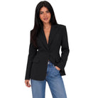 A woman modeling a black single-breasted blazer with notched lapels and flap pockets, paired with light-wash blue jeans, against a plain white background.