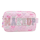 A pink quilted cosmetic pouch with 'MAKEUP' spelled out in glittery letters across the front, decorated with a bow pattern, on a white background.