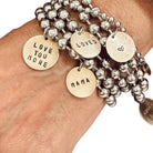 Stack of silver beaded bracelets with gold charm tags on a wrist.