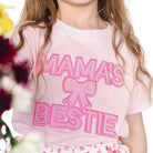 Child wearing a pink shirt with 'Mama's Beste' text and a bow graphic.