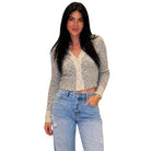 A woman modeling a cropped, long-sleeve knit cardigan in a heathered light gray and beige pattern with a cream ribbed trim and button placket, paired with light-wash blue jeans, against a plain white background.