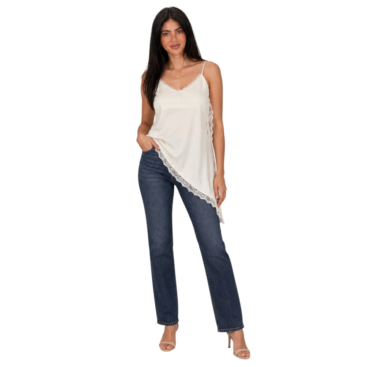 A woman modeling a white camisole top with lace trim and dark blue jeans against a plain white background.