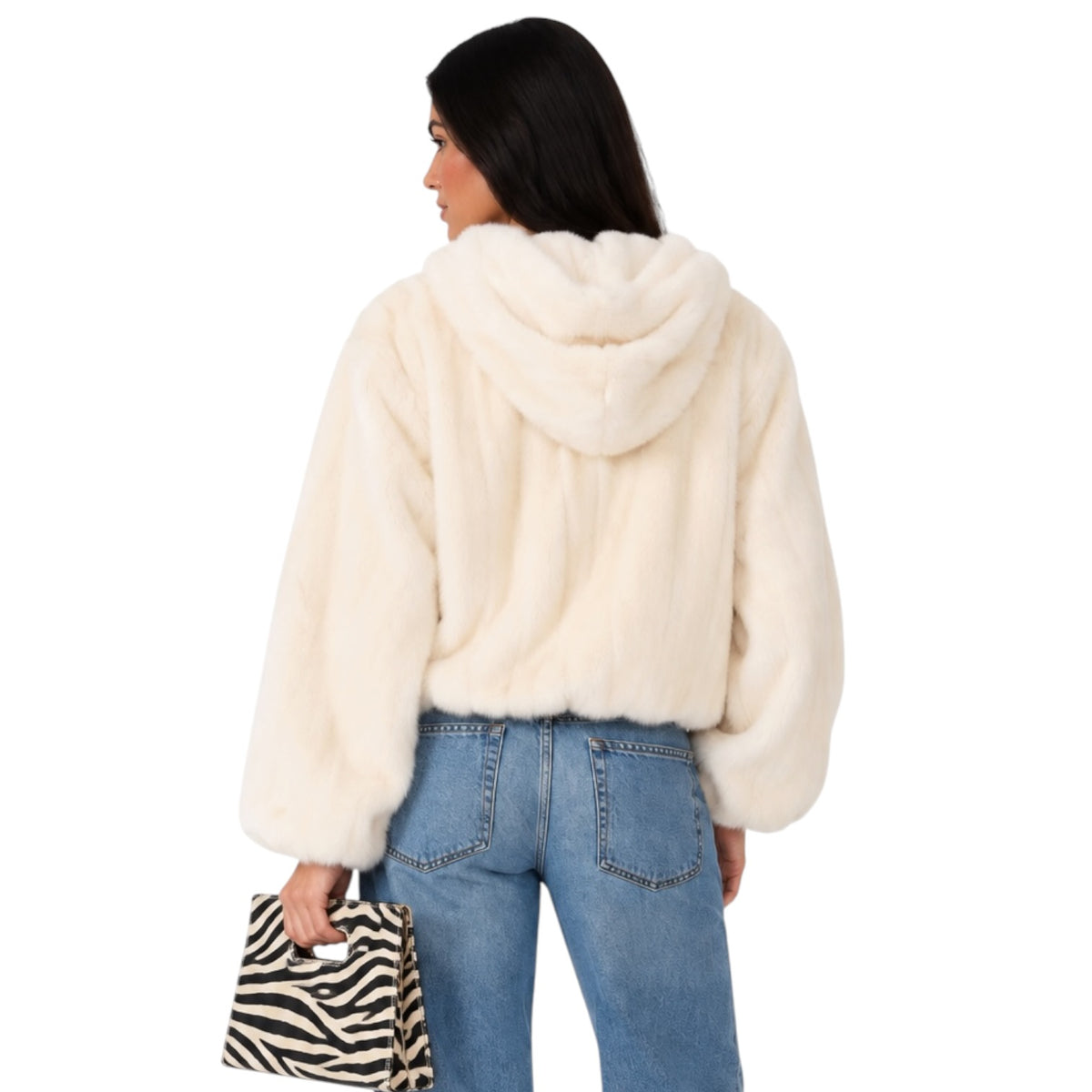 A woman shown from the back wearing a cream faux fur cropped hoodie with a hood, paired with blue jeans and holding a black and white zebra print clutch bag against a solid white background.