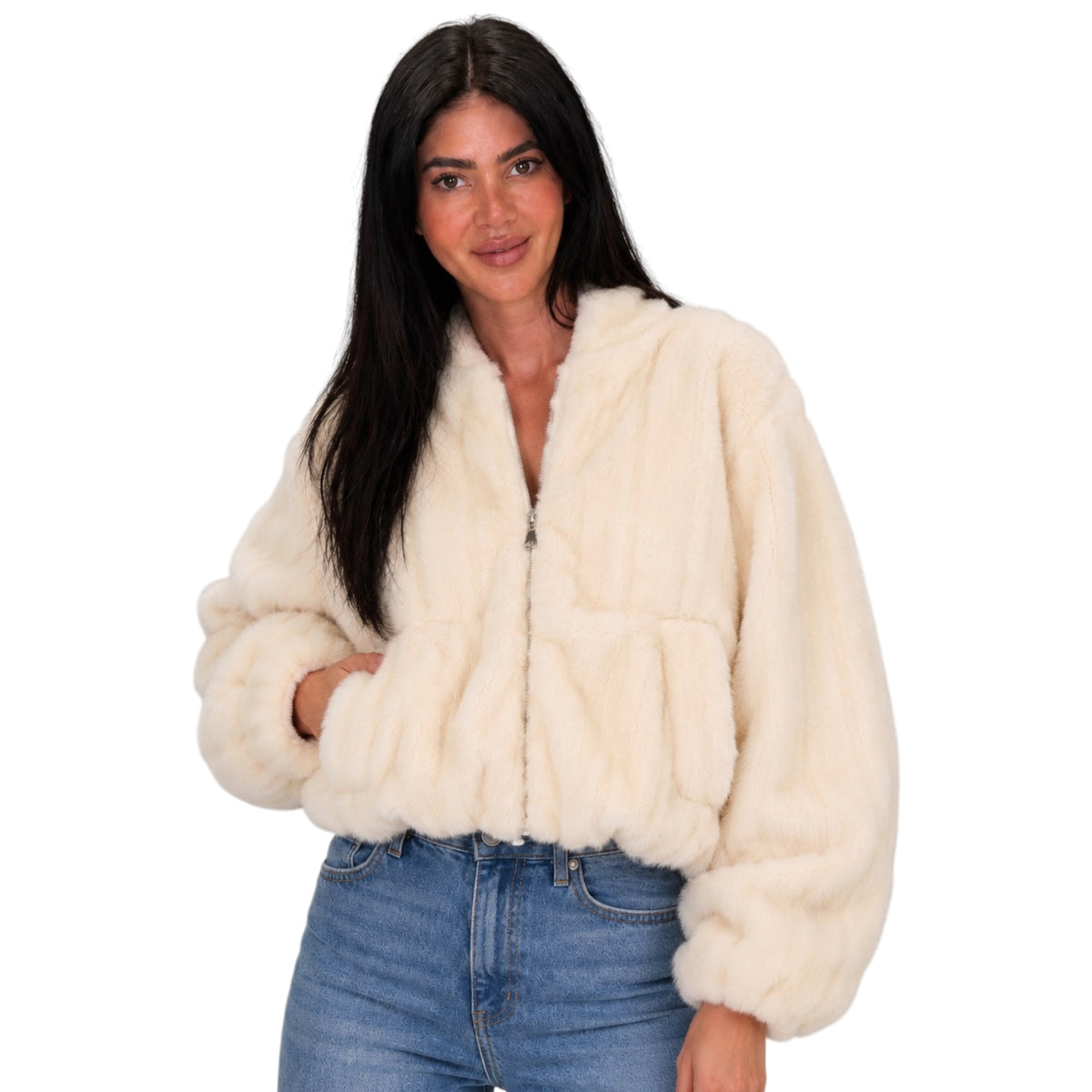 A woman modeling a cropped, cream-colored faux fur jacket with a front zipper and pockets, paired with blue jeans, against a solid white background.