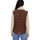 A woman shown from the back wearing a brown quilted puffer vest over a cream cable-knit turtleneck sweater and blue jeans, against a plain white background.