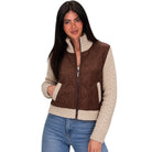 A woman modeling a brown quilted zip-front vest with cream cable-knit sleeves, ribbed collar and hem, paired with blue jeans against a plain white background.