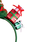A close-up of a green headband decorated with three miniature wrapped gift boxes in red, pink, and green, tied with red, green, and white ribbons, on a plain white background.