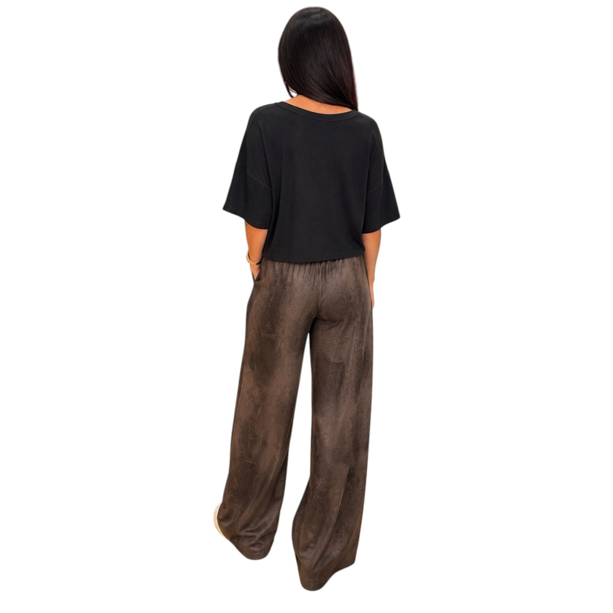 A woman shown from the back wearing a black short-sleeve top and brown wide-leg pants, standing against a plain white background.