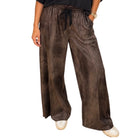 A person wearing wide-leg brown faux-leather pants with a black drawstring waist, paired with a black top and white sneakers, shown against a plain white background.
