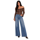 A woman modeling an off-the-shoulder brown ribbed knit top with a front zipper and wide-leg blue denim jeans against a plain white background.