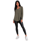A woman modeling a long-sleeve olive green V-neck top with black faux-leather leggings and white sneakers, set against a plain white background.