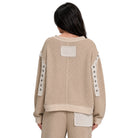 A person shown from the back wearing a beige textured knit sweater and matching pants with contrasting cream patchwork details and decorative buttons on the sleeves, against a plain white background.
