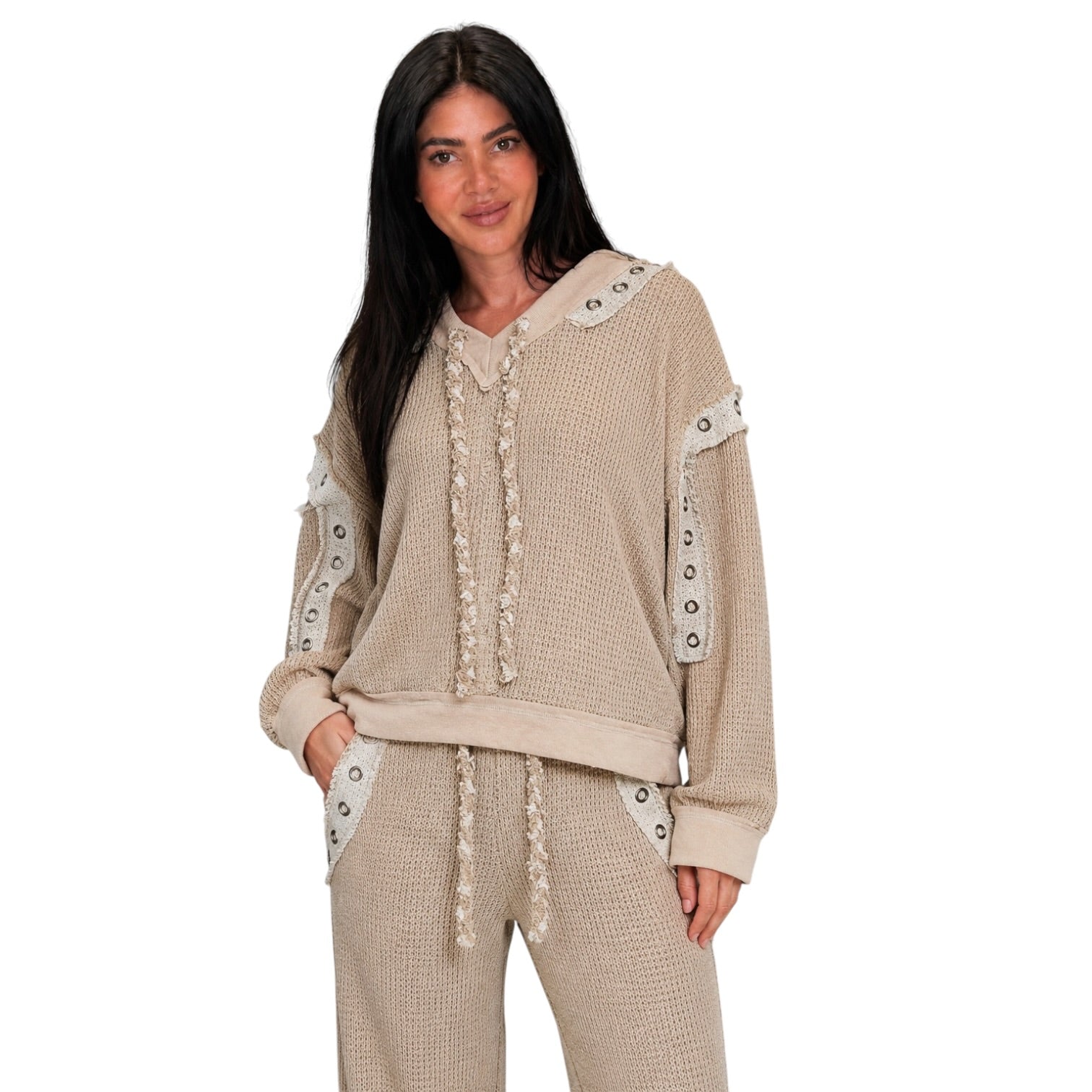 A woman modeling a beige waffle-knit lounge set consisting of a cropped hoodie with decorative lace-up front and grommet sleeve details, paired with matching jogger pants, against a solid white background.
