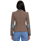 A woman viewed from the back wearing a brown and black diagonally striped blazer with blue denim elbow patches and a blue denim collar, paired with blue jeans against a white background.
