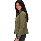 A woman wearing an olive green cropped jacket with denim trim details, paired with dark jeans, shown from a side profile against a plain white background.