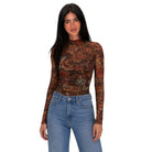A woman modeling a long-sleeve mock neck bodysuit with a brown, rust, and orange floral pattern, paired with blue jeans, against a plain white background.