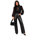 A woman modeling a black sheer long-sleeve top with a deep V-neck, paired with black faux-leather wide-leg pants, holding a black handbag against a plain white background.