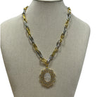 A two-tone gold and silver chain necklace with a circular pendant, displayed on a beige fabric jewelry bust against a white background.