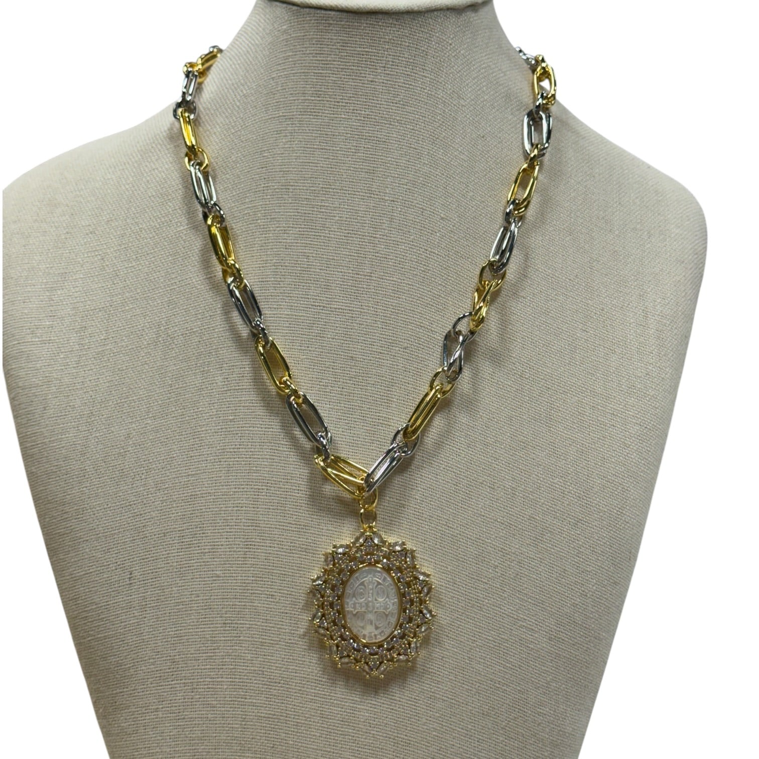 A two-tone gold and silver chain necklace with a circular pendant, displayed on a beige fabric jewelry bust against a white background.