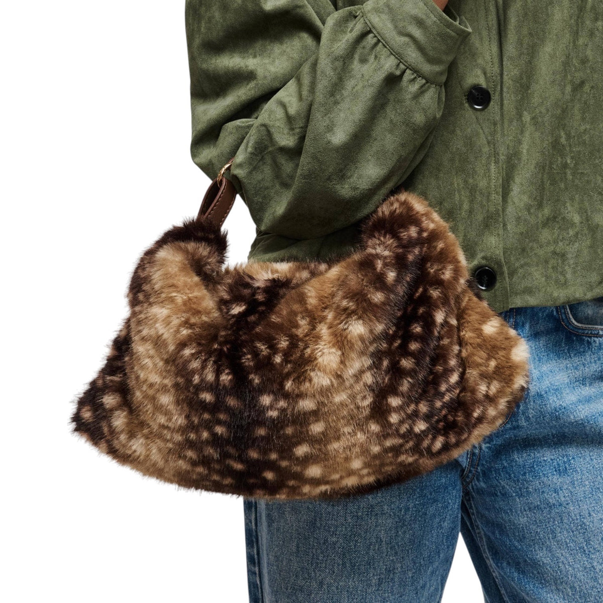 A person wearing an olive green jacket and blue jeans holds a brown and beige spotted faux fur shoulder bag against a white background.