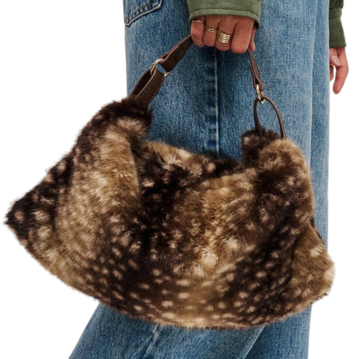 A person wearing blue jeans and an olive green top holds a large brown faux fur shoulder bag with white spots, resembling a dalmatian pattern, against a white background.