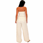 A woman shown from the back wearing a strapless cream-colored jumpsuit with a textured, ribbed knit fabric and wide legs, set against a plain white background.
