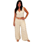 A woman modeling a two-piece cream crochet or lace outfit consisting of a sleeveless cropped top with a front zipper and matching wide-leg pants with ruffled trim, set against a plain white background.